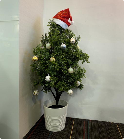 Small decorated Christmas tree with ornaments and Santa hat in Netmore office, showing a cheerful and creative career environment in Malaysia.